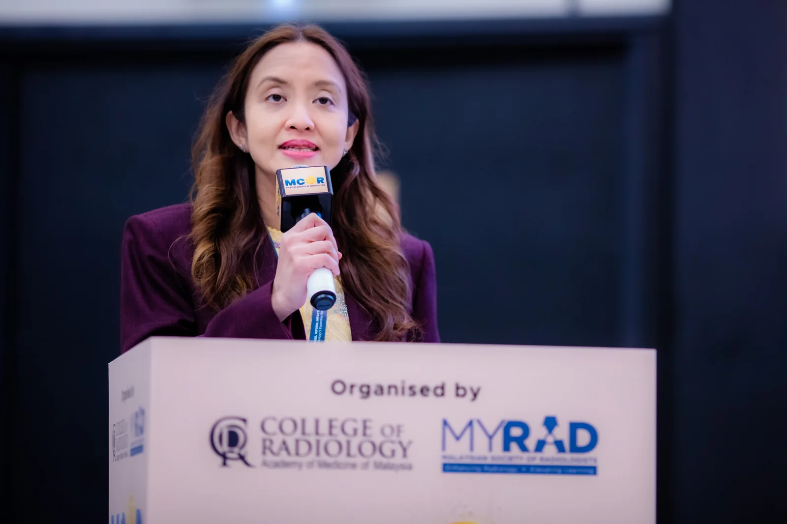Dr Farhana Fadzli holding a microphone while speaking at a lectern.