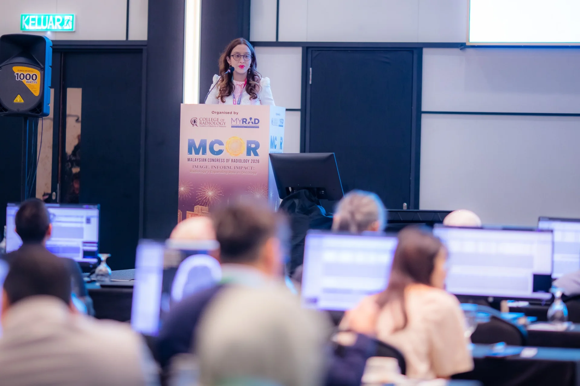 Dr Farhana Fadzli speaking at a lectern before a professional audience.